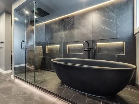 Black freestanding tub beside a glass-enclosed shower with lit niches in a Redmond, WA basement bathroom