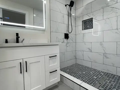 Walk-in shower with white marble-look tile and a black hexagon pebble floor beside a white vanity