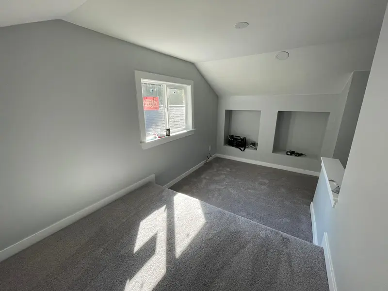 Carpeted attic room with a gable window and two lit wall niches in the side wall