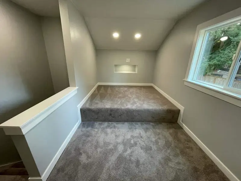 Raised carpeted landing in the attic with a side window and recessed lights