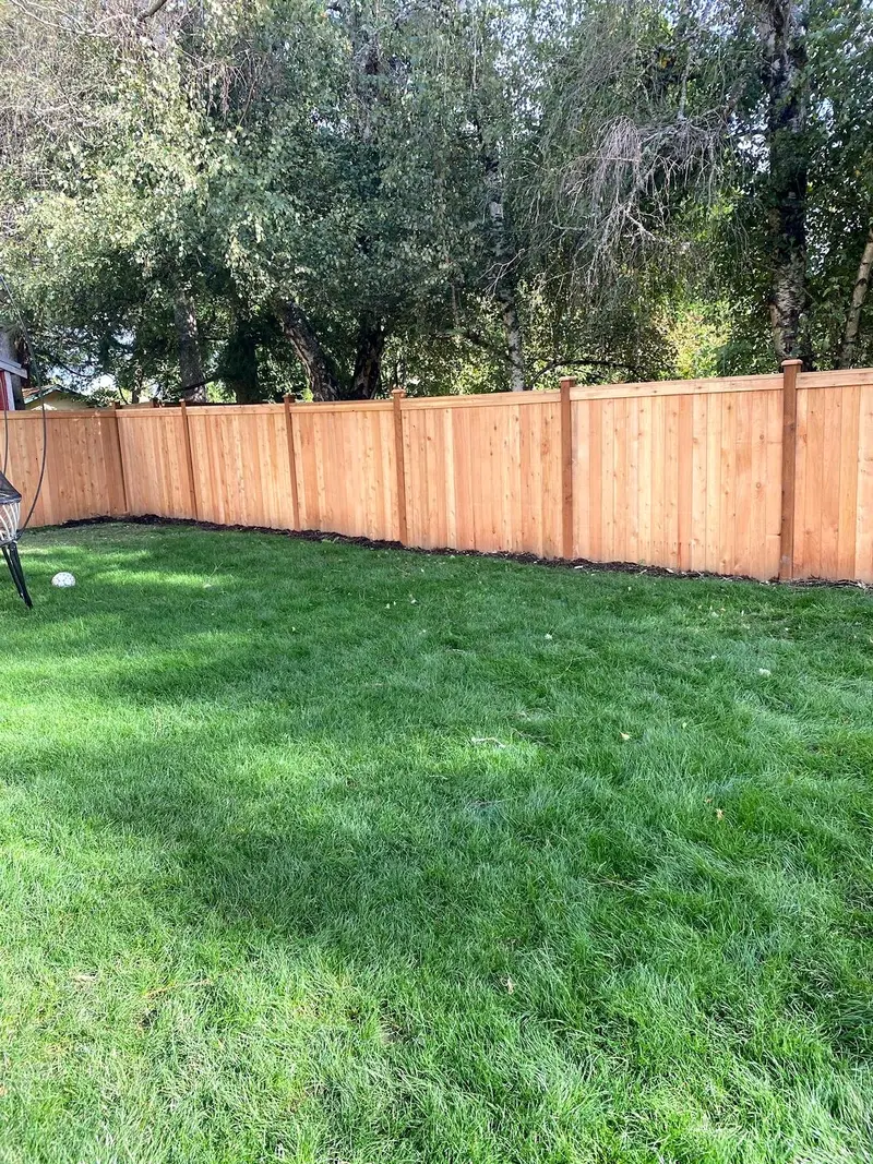 Flat-top cedar fence with posts between each section turning a corner around a green lawn under tall trees