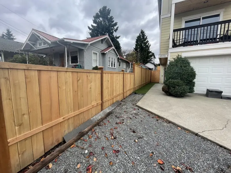 New cedar fence along the driveway with a strip of gray gravel at its base