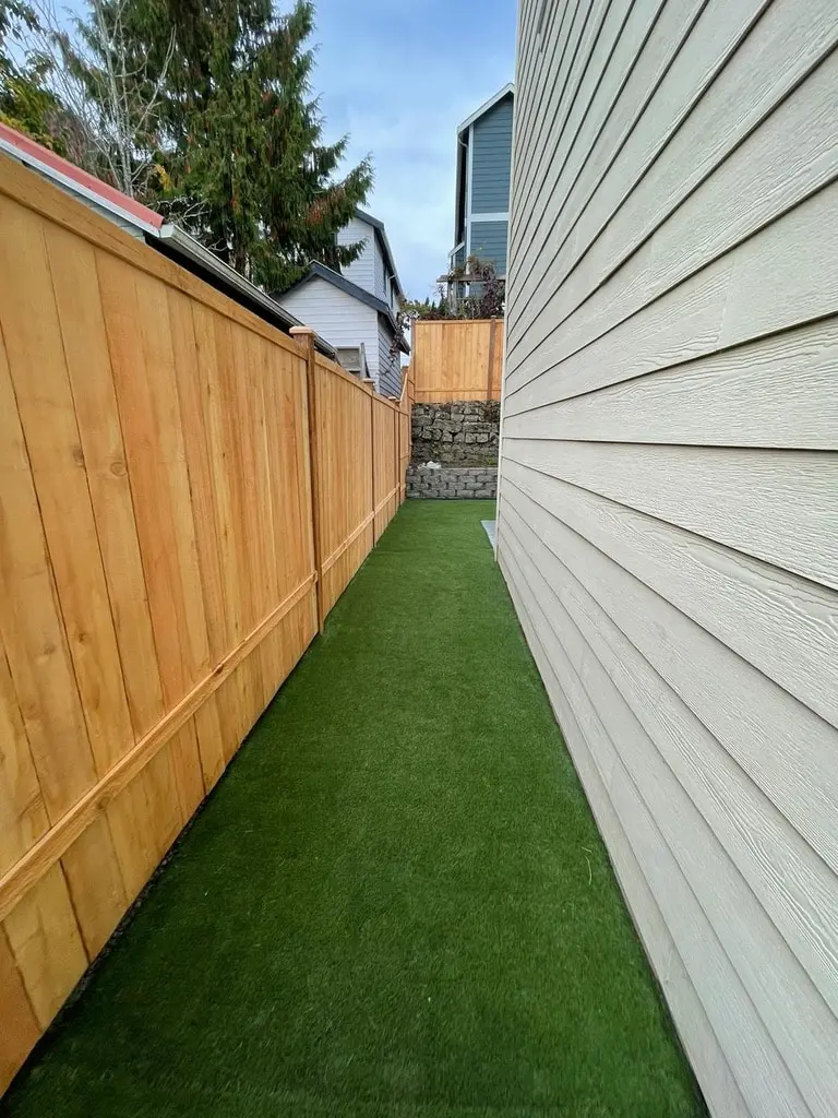 Side yard covered in artificial turf between the house siding and a new cedar fence