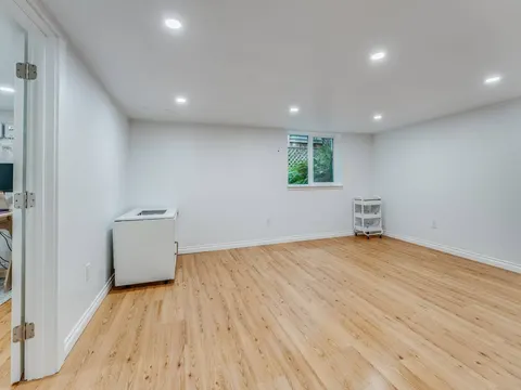 Open finished basement room in Seattle, WA with white walls, recessed lights, a small window and oak look flooring