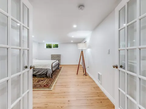 Glass French doors open onto a finished basement bedroom in Seattle, WA with a floor lamp and light plank flooring