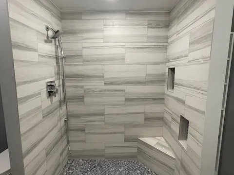 Basement walk in shower in Federal Way, WA with gray plank tile walls, niches, a bench and a pebble floor