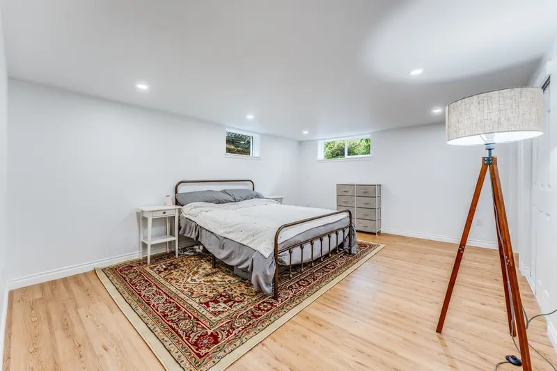 Basement bedroom with a bed and a patterned rug under two high windows