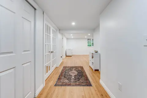 Long basement hallway with white walls, closets and a runner rug on the plank floor
