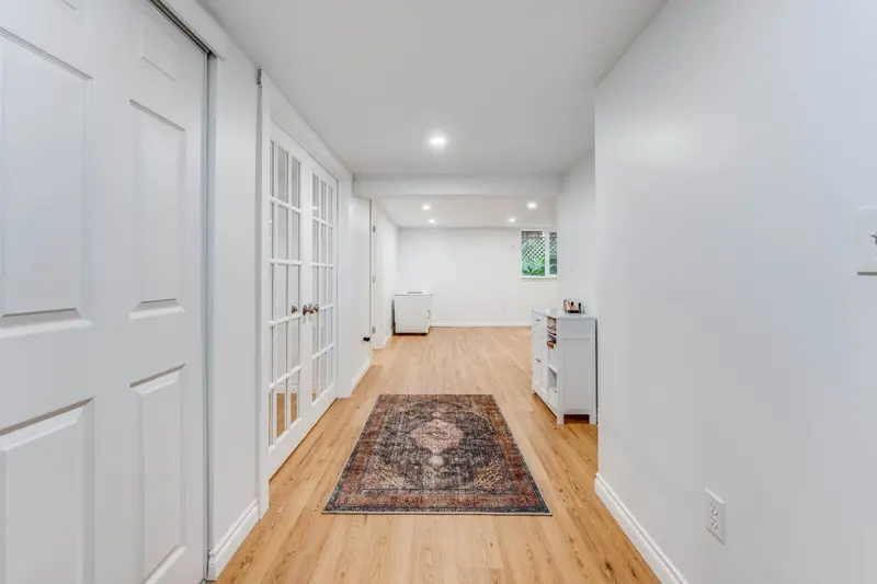 Long basement hallway with white walls, closets and a runner rug on the plank floor