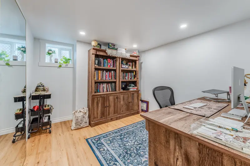 Basement room with a wood bookshelf and a desk on a blue rug by a small window