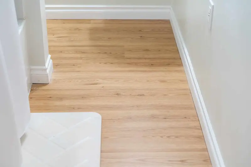 Light plank floor meeting the bottom of the basement stairs with a white riser