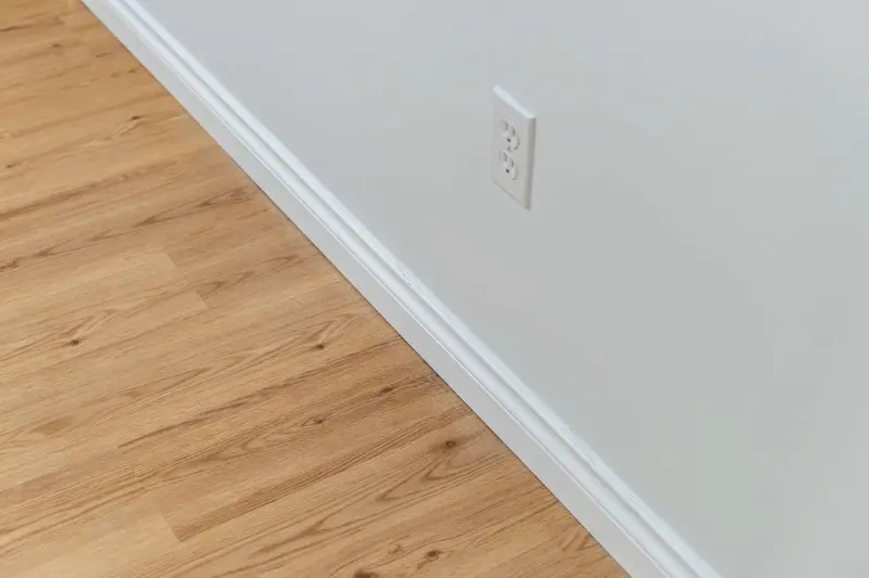 Close view of a new white baseboard meeting a light oak-look plank floor