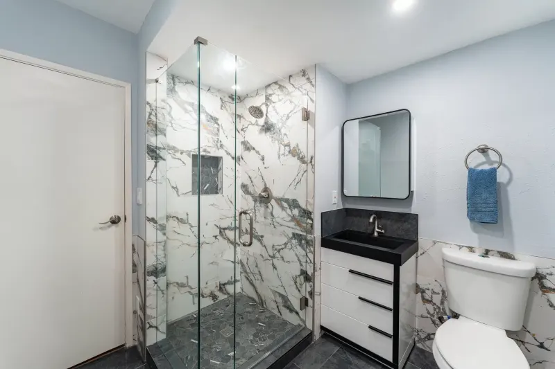 Remodeled bathroom in Bellevue, WA with a frameless glass shower, marble look porcelain tile and a white vanity with a black top