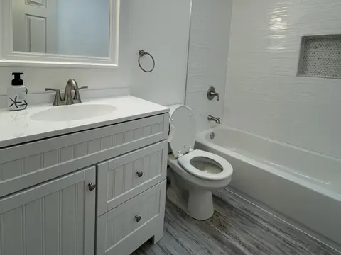 Hall bathroom in Bothell, WA with a gray vanity, a white tub with wave pattern wall tile and a gray plank floor
