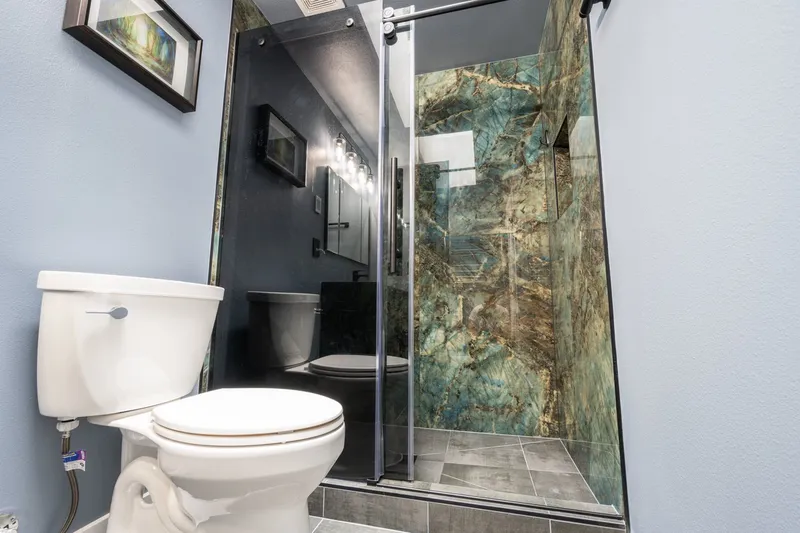 Glass shower with blue and green stone look wall panels beside a white toilet in a remodeled bathroom in Everett, WA