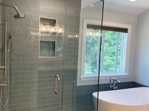 Green glass tile shower with two niches beside a freestanding tub in Snohomish, WA