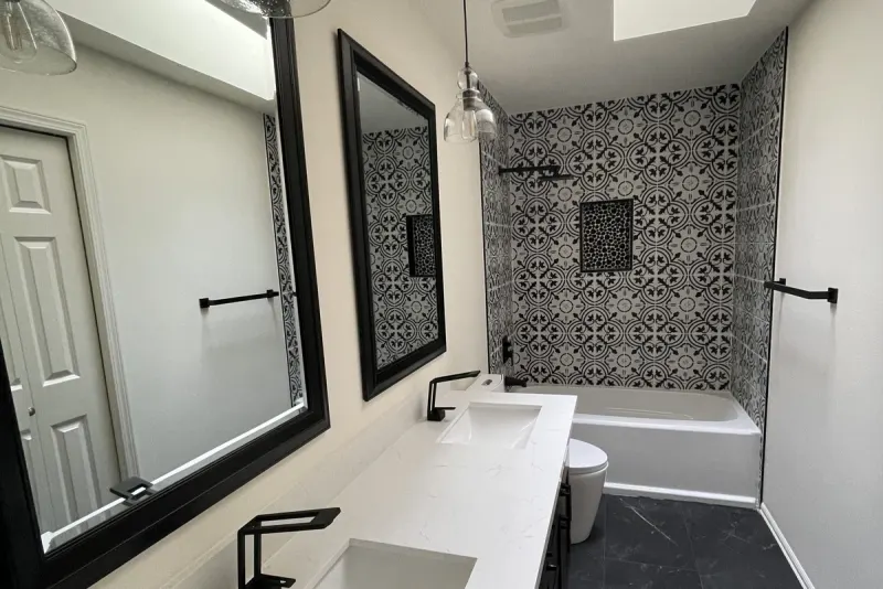 Double vanity with a white quartz top, black faucets and framed mirrors under a skylight, facing a tub wall of black and white patterned tile in Issaquah, WA