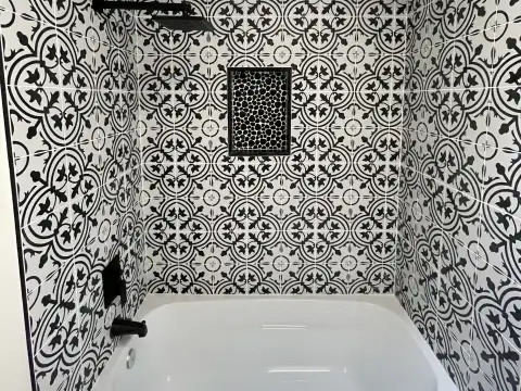 Alcove tub surrounded by black and white patterned tile, with a matte black shower head and a pebble tile niche, in Issaquah, WA