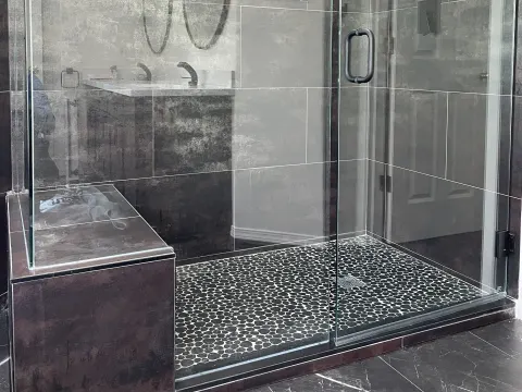 Frameless glass walk in shower with dark large format tile, a tiled bench and a pebble floor in Issaquah, WA