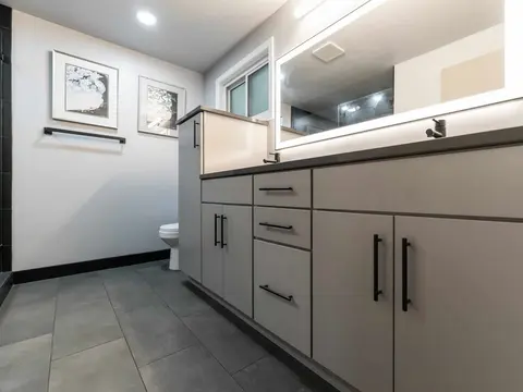 Long gray vanity with black pulls, a lit mirror and a porcelain plank floor in Kirkland, WA