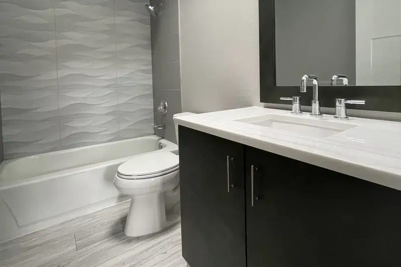 Remodeled bathroom in Kirkland, WA with a sculpted wave tile wall over the tub, a dark vanity with a white stone top and plank flooring
