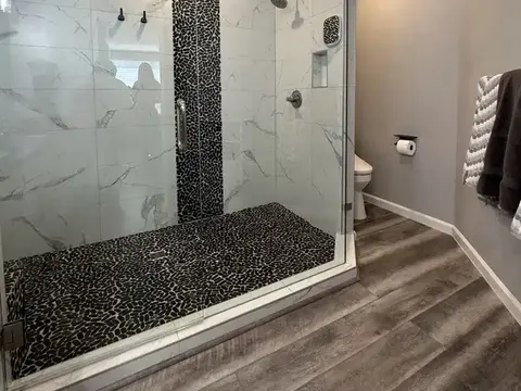 Glass walk in shower with marble look tile, a black pebble floor and a pebble accent stripe in Kirkland, WA