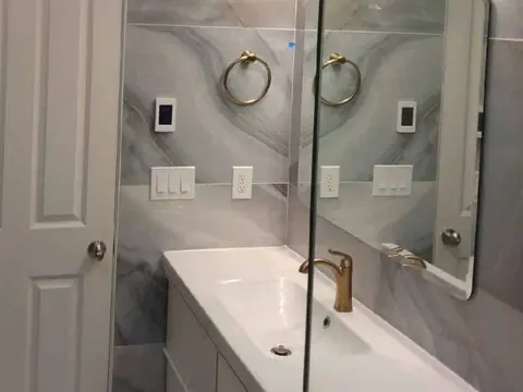 Gray marble look tile wall with a brass towel ring, a brass vanity light bar and a white floating vanity in Monroe, WA