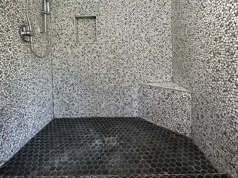 Walk in shower with pebble tile walls, a tiled bench and a black hexagon tile floor in Gold Bar, WA