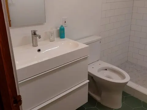 White floating vanity and toilet on green hexagon floor tile under a sloped ceiling in Seattle, WA