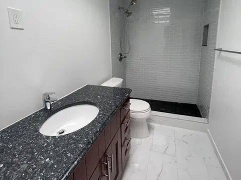 Granite topped vanity beside a glass tile shower with a black pebble floor in Seattle, WA