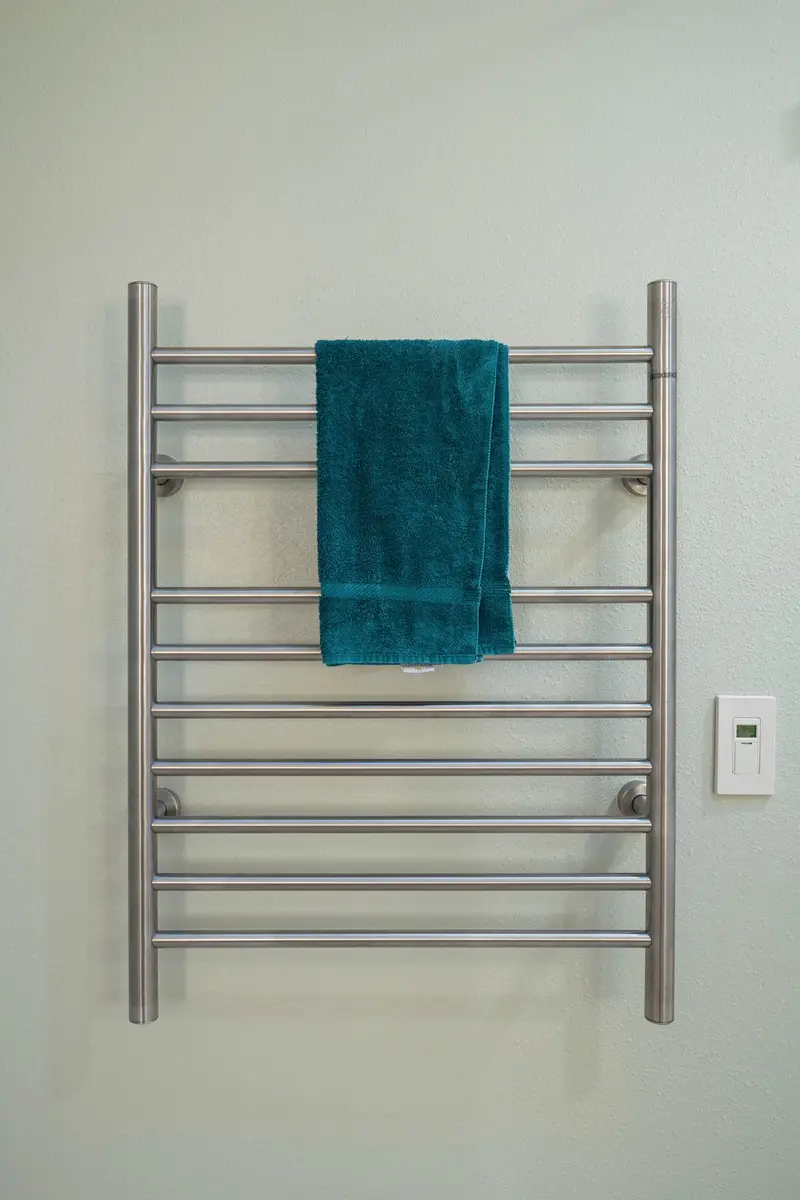 Brushed steel heated towel rail with a teal towel and a wall switch