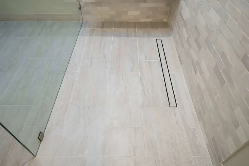 Linear drain along the shower wall in wood-look floor tile, with the glass panel at the edge
