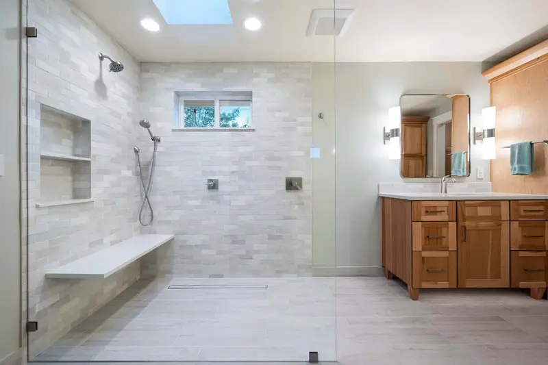 Master bathroom with an open glass walk-in shower, floating bench and skylight beside a wood shaker vanity