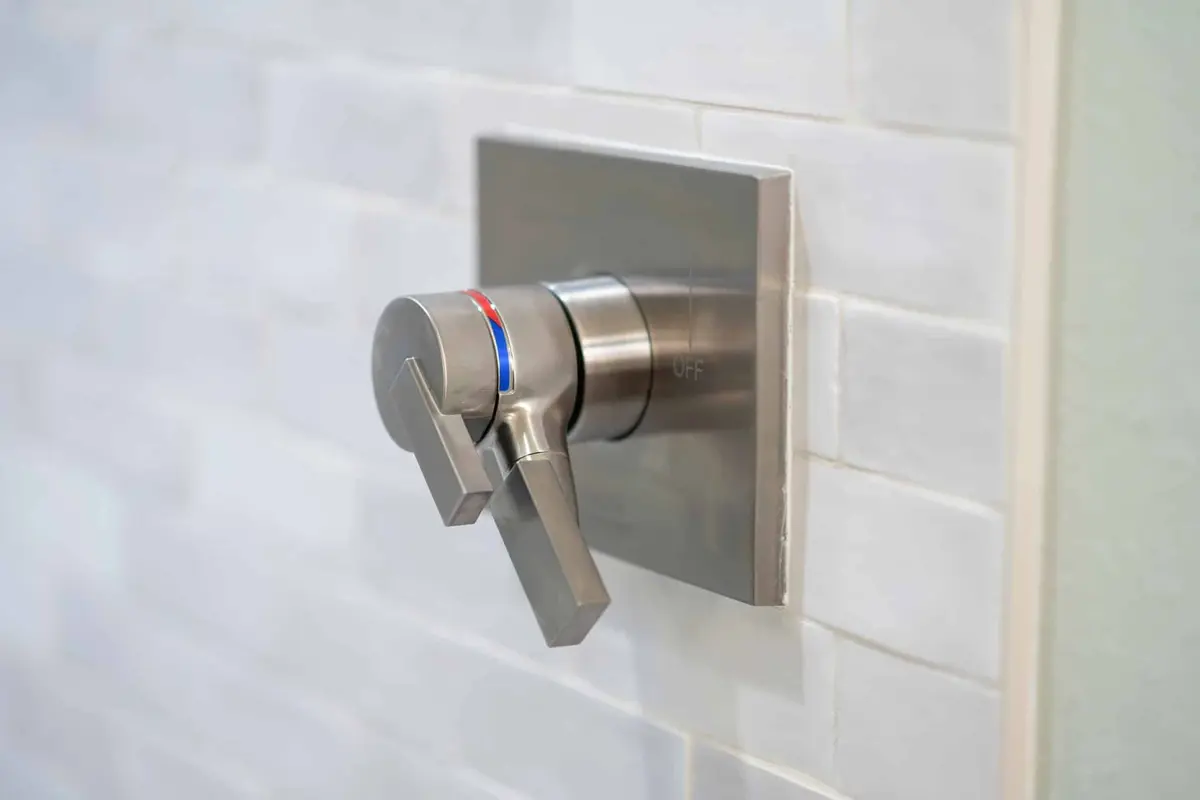 Brushed nickel shower valve trim with two lever handles set in light handmade-look tile