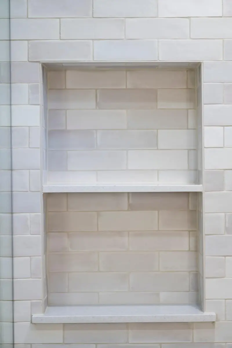 Close view of a tiled shower niche divided by a white shelf
