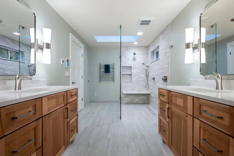 Two wood shaker vanities on either side of the room with the walk-in shower and skylight between them