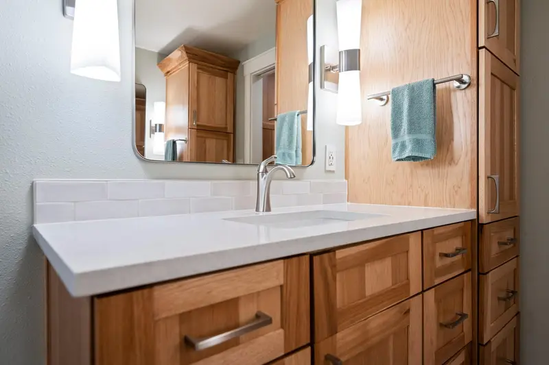 Wood vanity with an undermount sink, two tall wall sconces and a rounded mirror