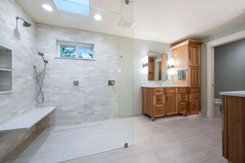 Walk-in shower under a skylight with a window, a floating white bench and a niche in light tile