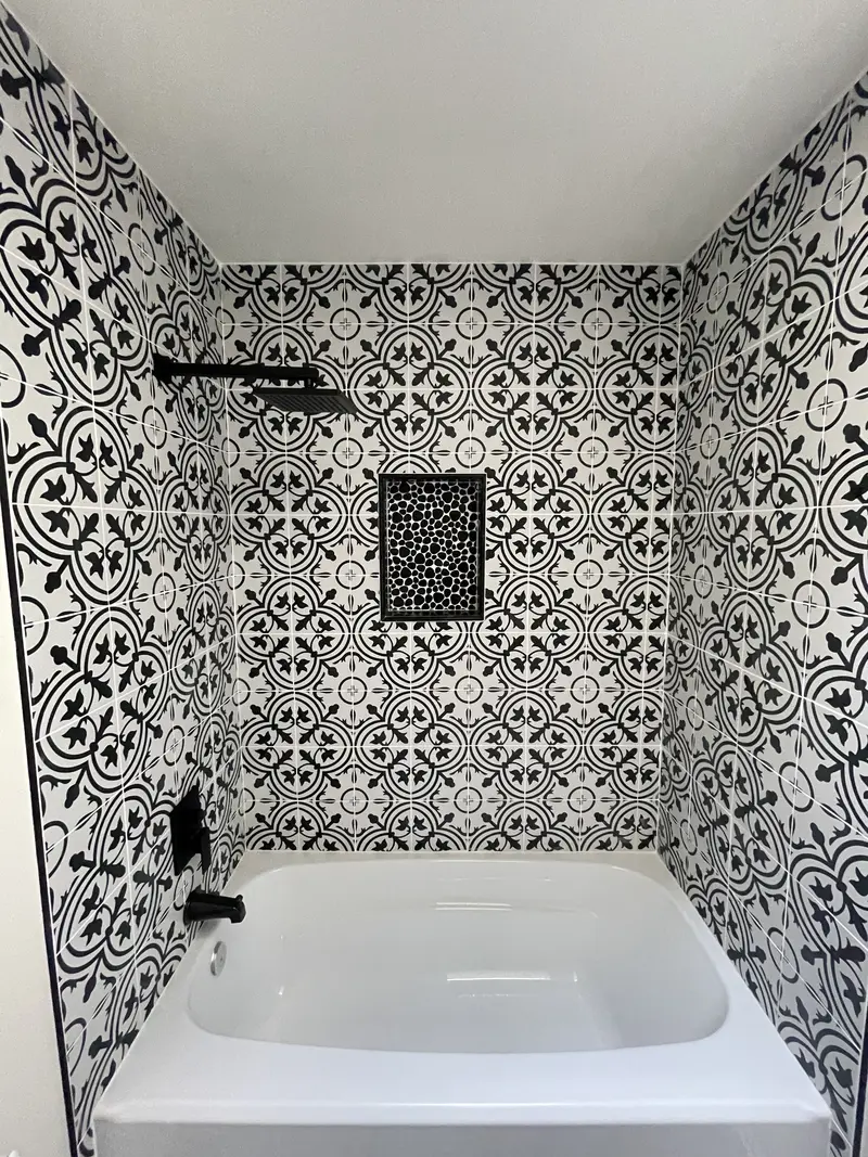 White tub surrounded by black and white patterned tile with a black niche and black shower fixtures