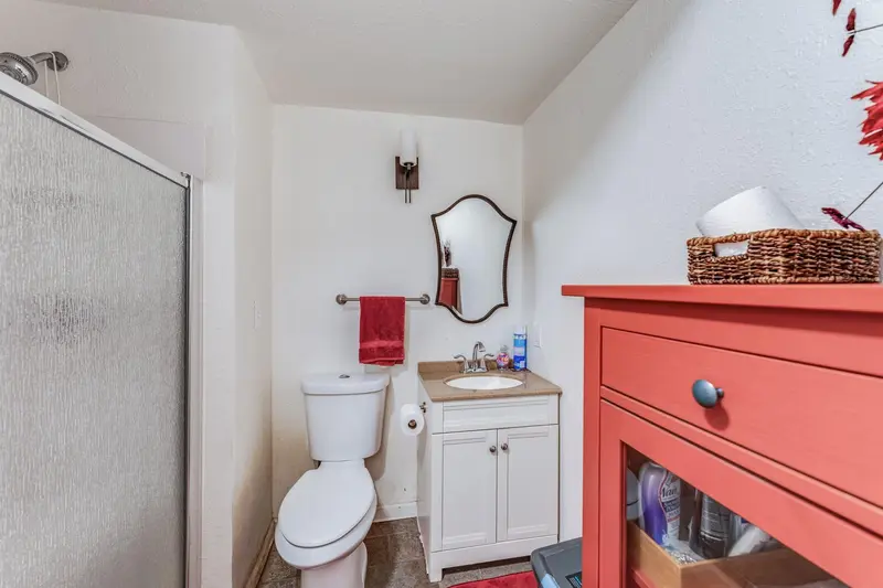 Small bathroom before the remodel with a frosted glass shower stall, a toilet, a white vanity and a red side cabinet