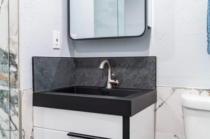 White vanity with an integrated matte black sink, slate-look backsplash and a black-framed mirror