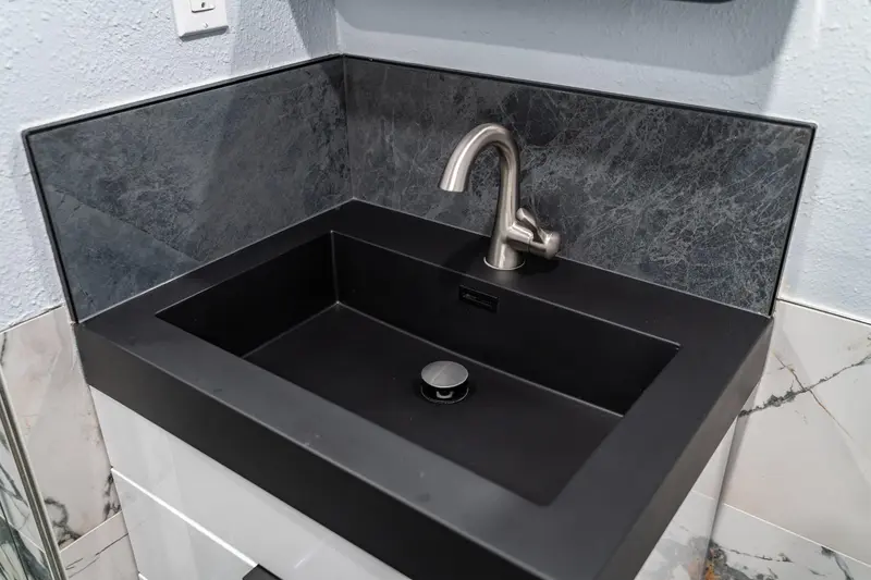Close view of a matte black integrated sink with a brushed nickel faucet and a dark tile backsplash