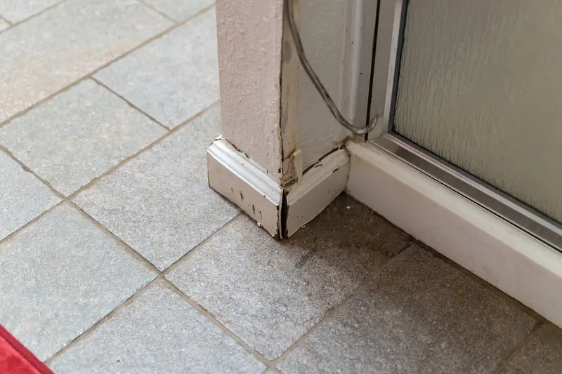 Damaged door trim and gray floor tile at the old shower stall entrance