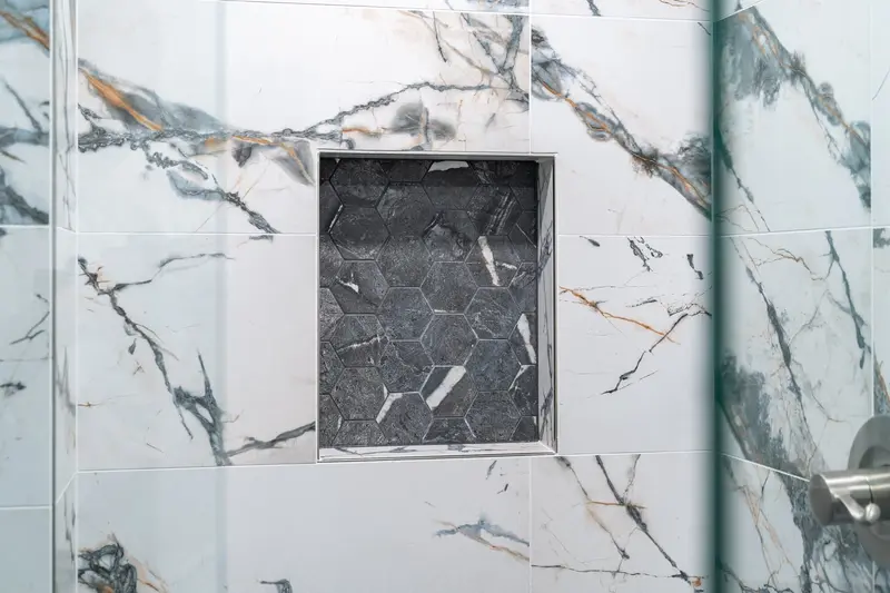 Shower niche lined with dark slate-look tile inside white marble-look walls
