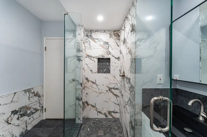 Frameless glass shower panels and a door handle in front of marble-look shower tile