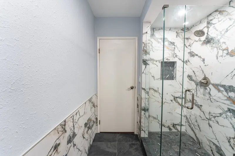 Walk-in shower with marble-look tile seen from beside the bathroom door