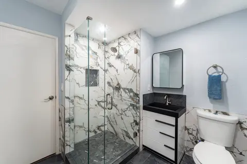 Frameless glass shower door beside a white vanity, black-framed mirror and toilet