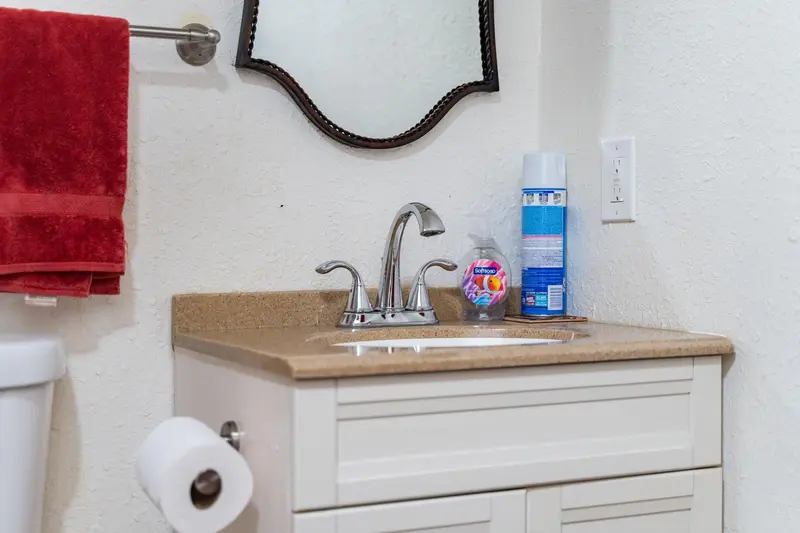 Old white vanity with a tan countertop, a chrome faucet and a decorative mirror