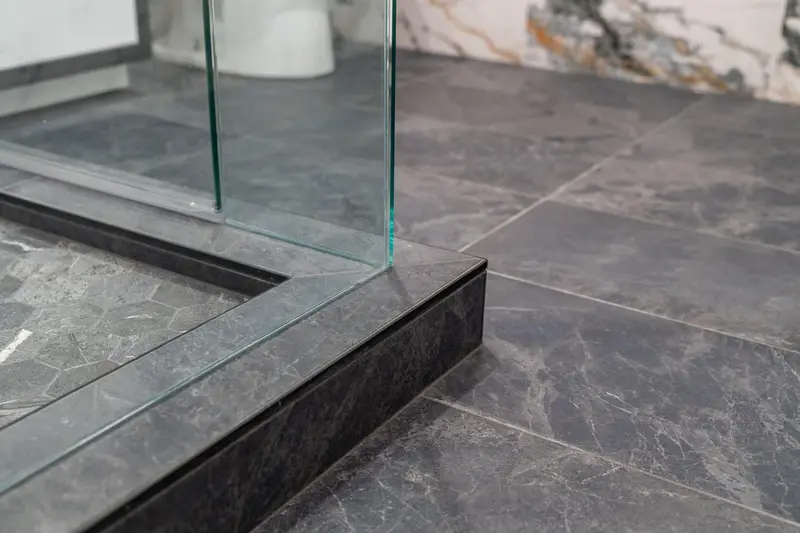 Shower curb finished in dark tile meeting the glass panels and the slate-look floor