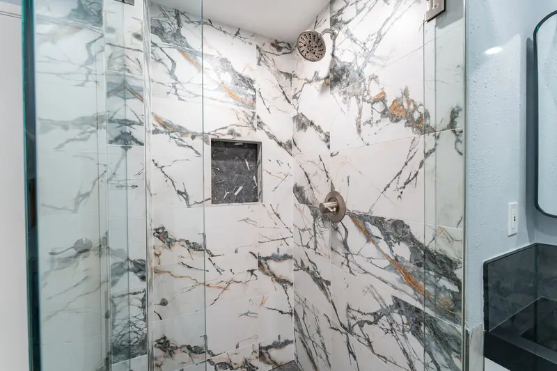 Marble-look tile shower wall with a recessed niche and a brushed nickel shower head